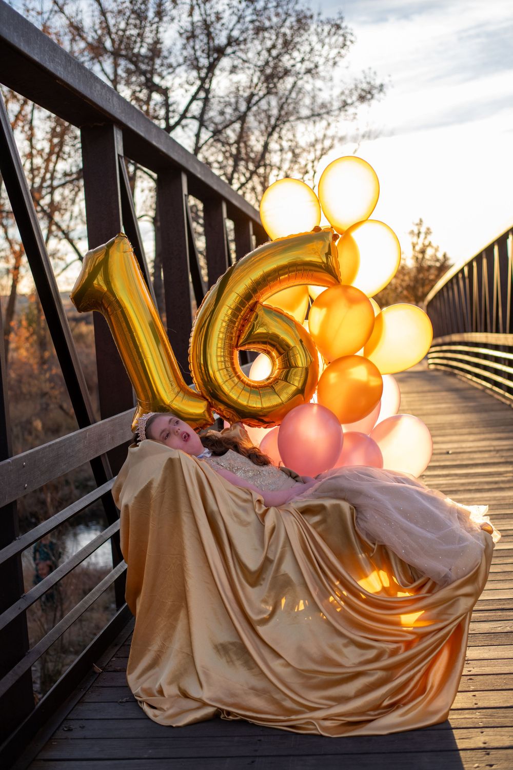 Number 16 balloon display with orange and pink balloons on bridge at sunset.