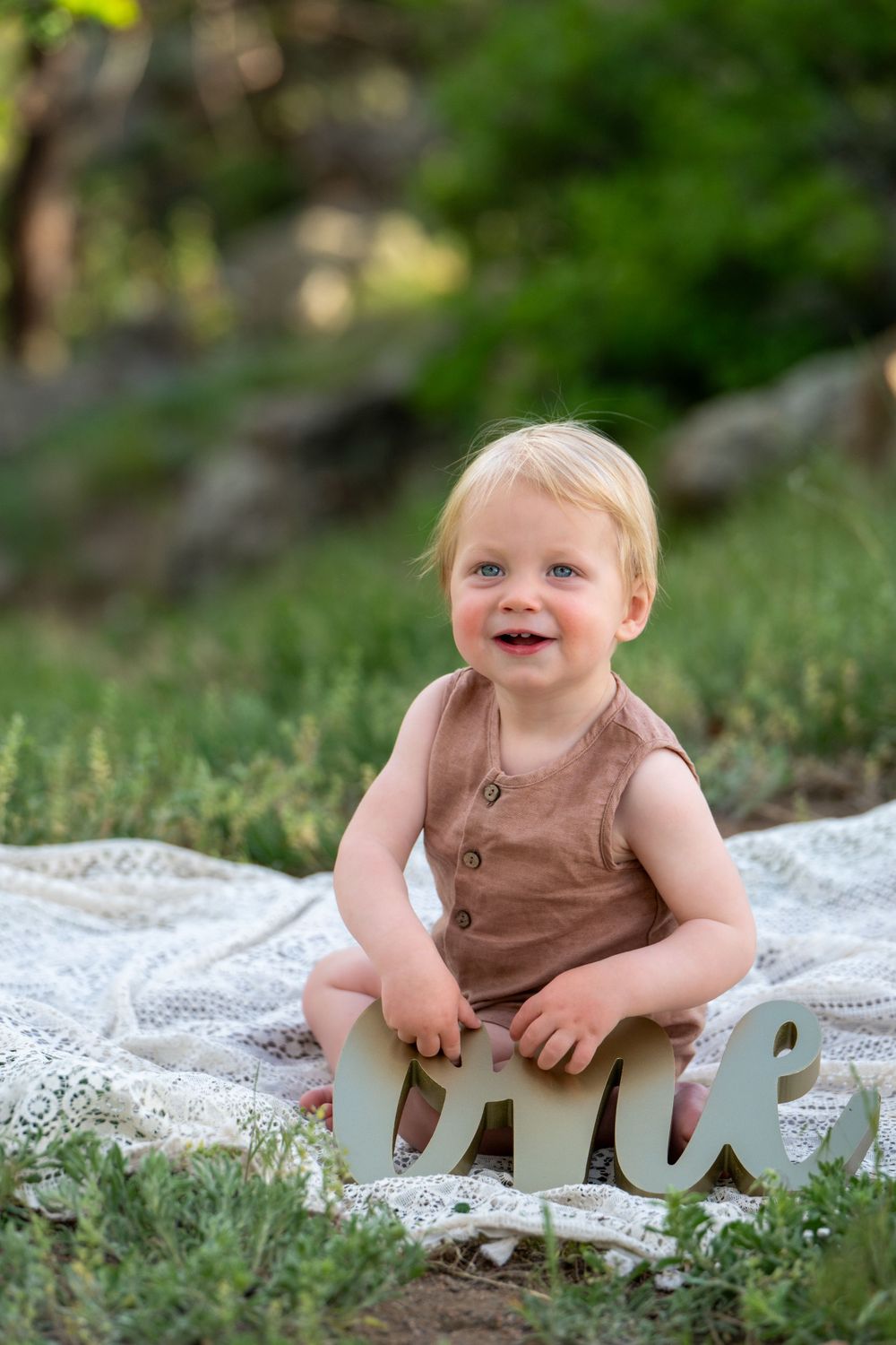 Outdoor portrait session with decorative 'one' text prop on lace blanket. Cake smash