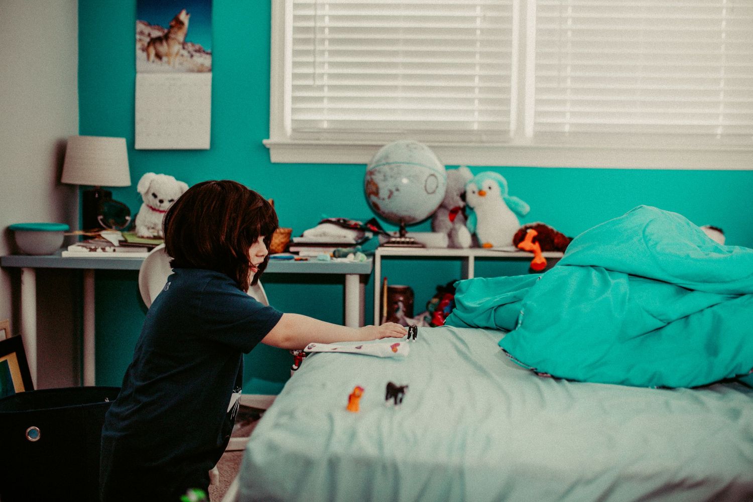 Child plays in a turquoise-themed bedroom decorated with stuffed animals and toys. Whitney Popp photographer