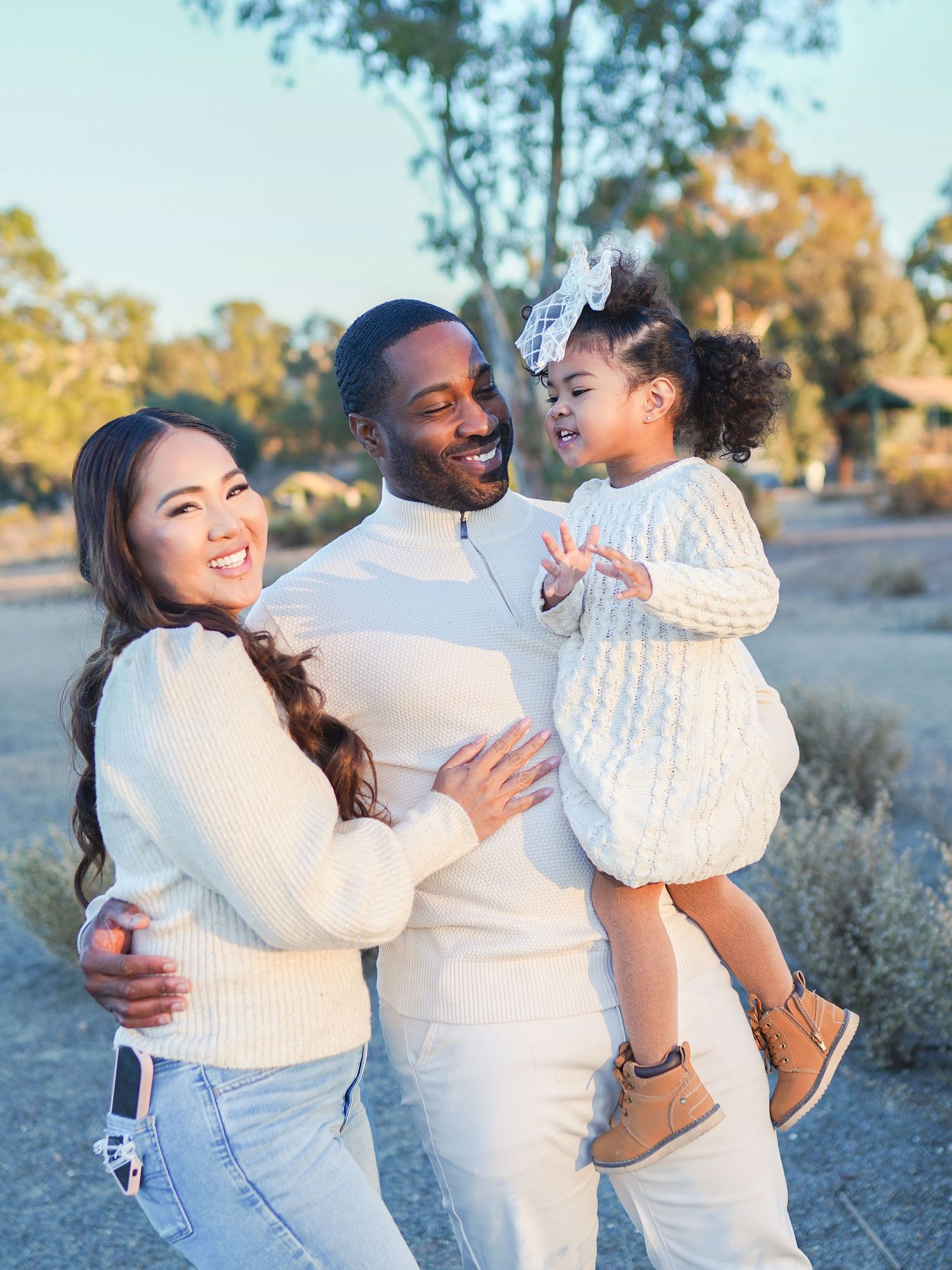 Family in coordinating cream sweaters poses together on nature trail.