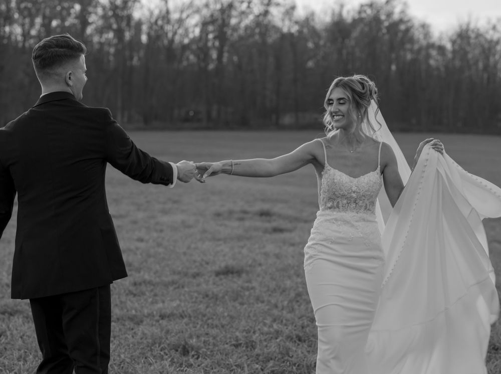 Romantic black and white photo of newlyweds dancing in an open field with trees in the background.