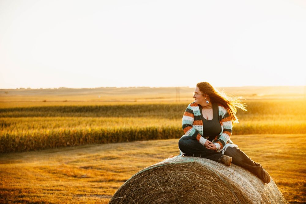 A romantic couple sits on a rustic wooden fence overlooking golden wheat fields at sunset.