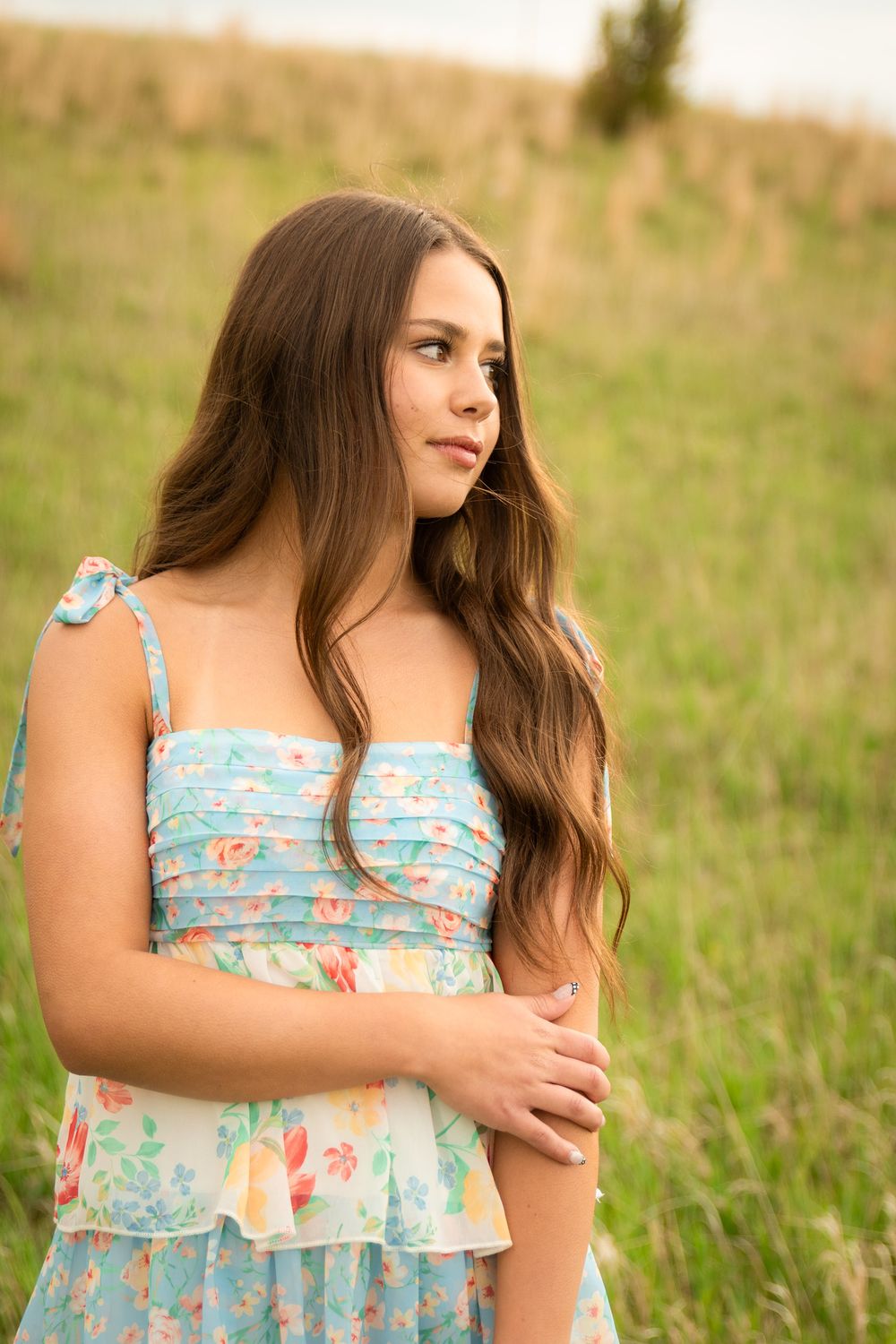 A series of outdoor portrait shots showing someone in a light blue floral sundress standing in a sunny meadow.