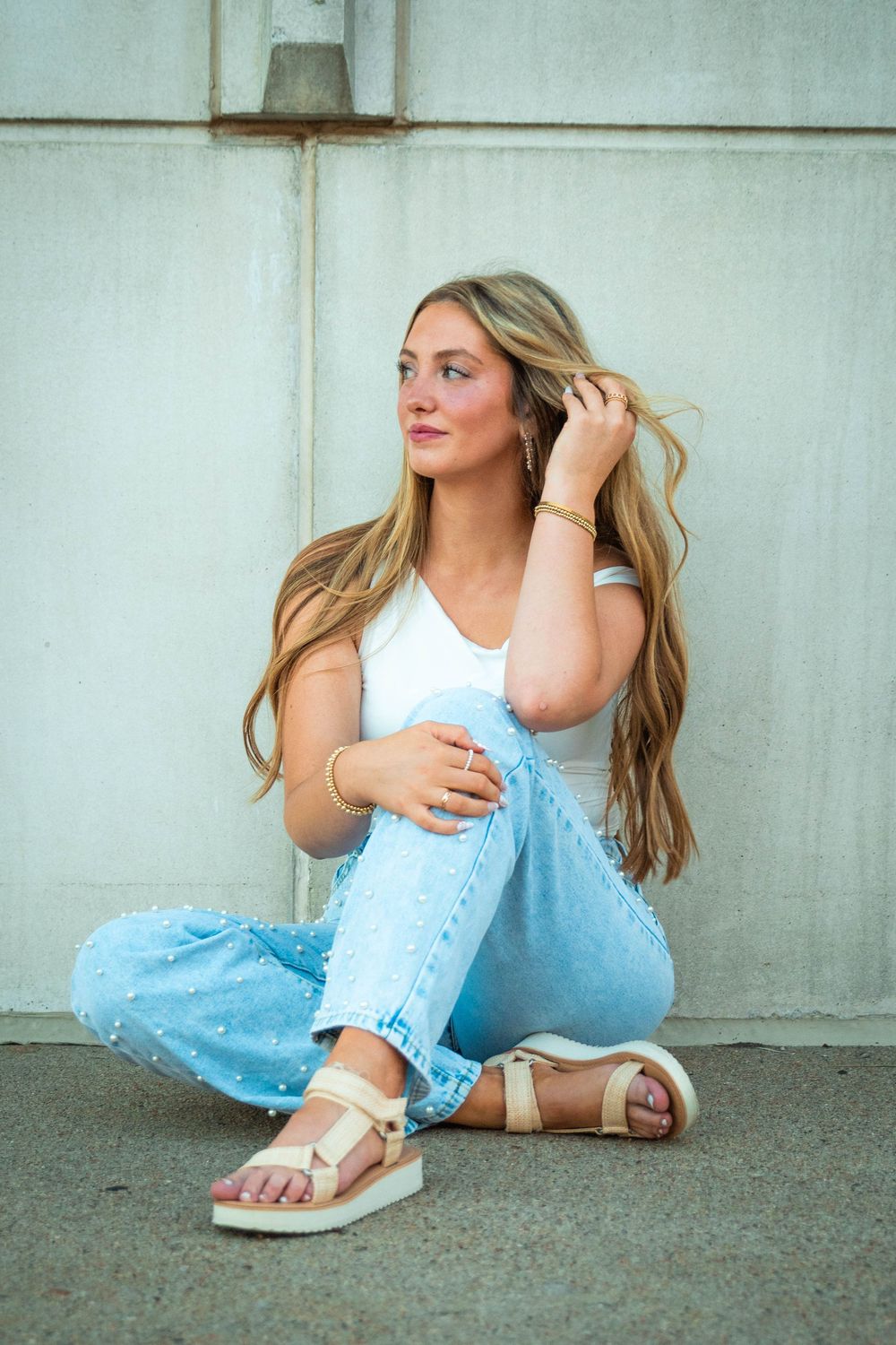 A series of fashion poses on the ground wearing a white crop top, light blue polka dot pants and gold sandals.