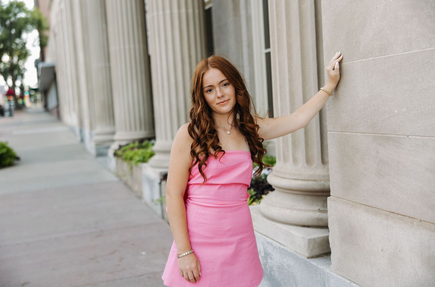 Person in pink dress standing against classical building columns outdoors.