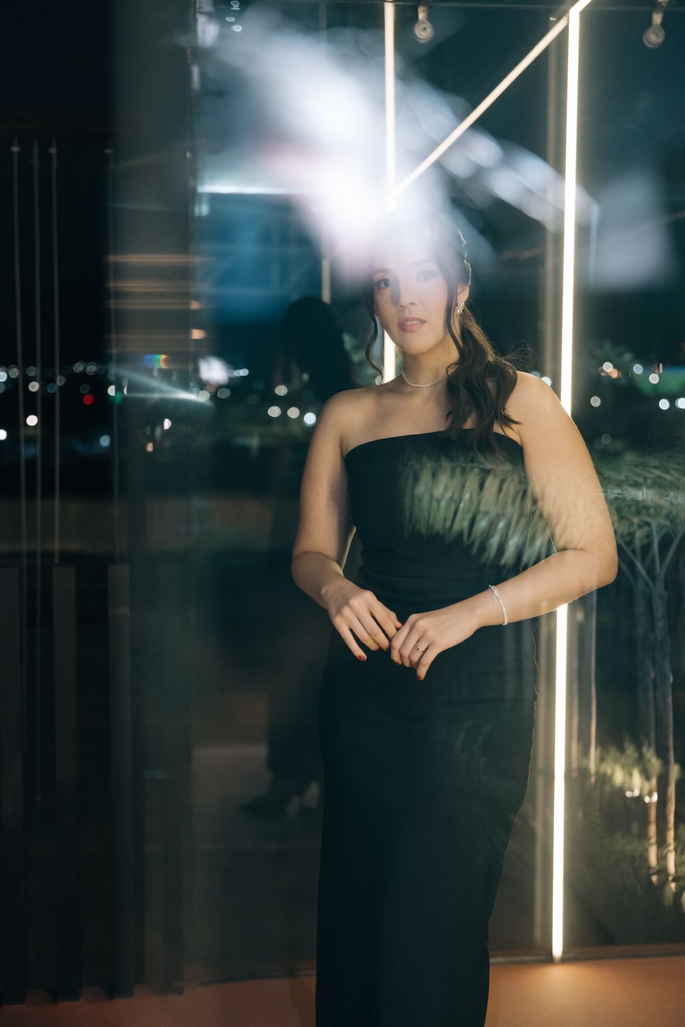 A person in black clothing poses in moody lighting with vertical light beams creating a dramatic nighttime atmosphere.