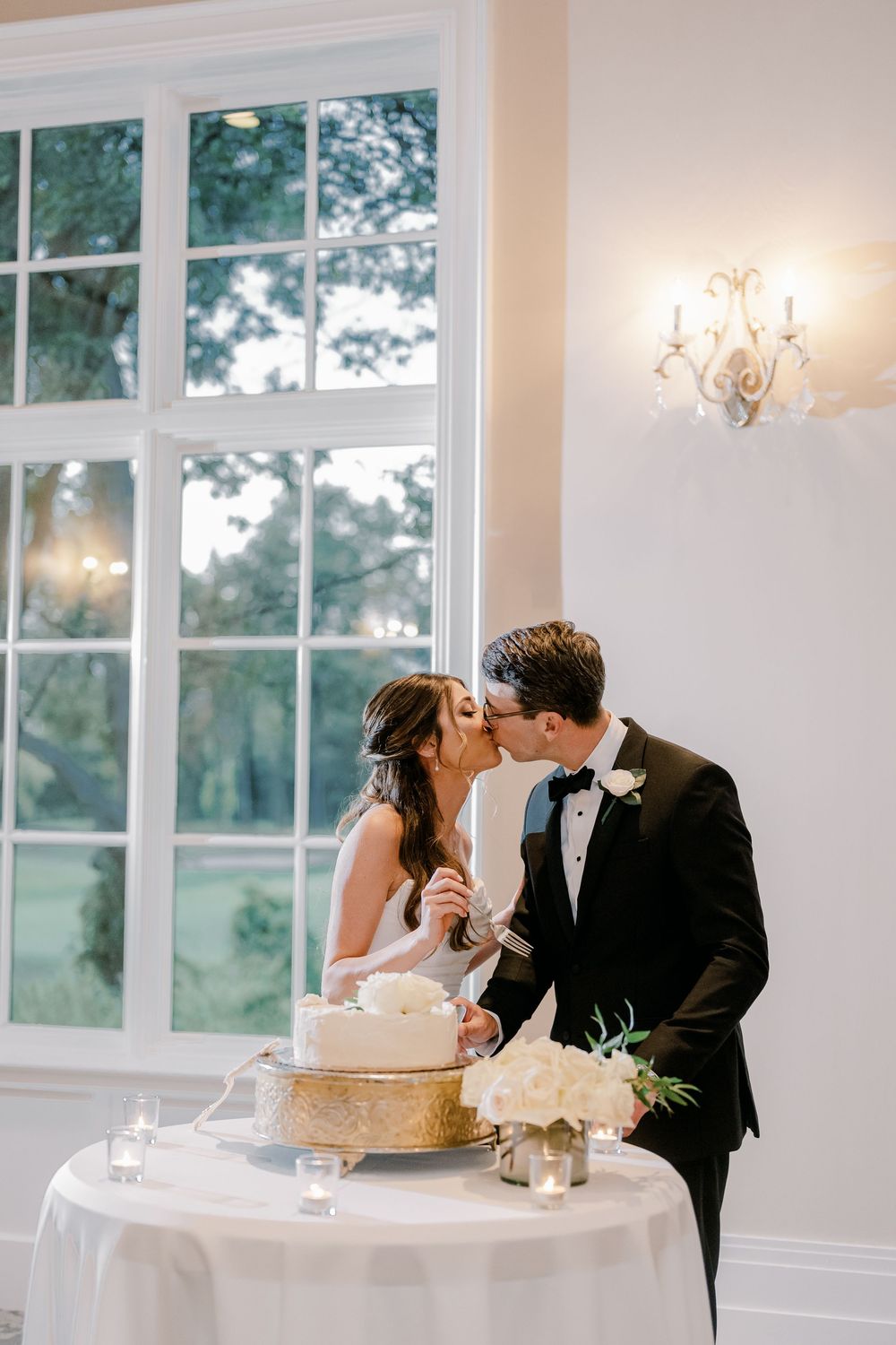 Wedding reception scene with cake cutting and champagne toast in an elegant white room.
