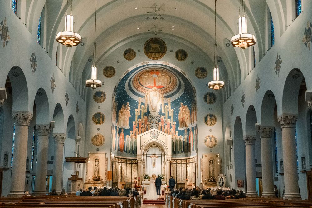 Panoramic view of an ornate Catholic church interior with blue ceiling and golden altar during a wedding.