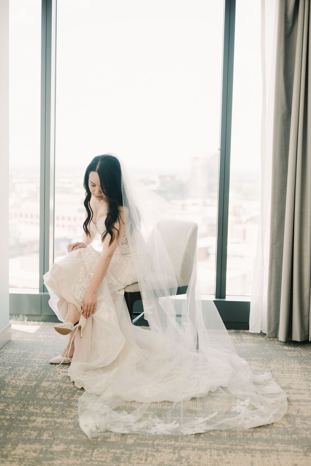 Bride in flowing white wedding dress poses elegantly by window in modern interior at hilton downtown columbus