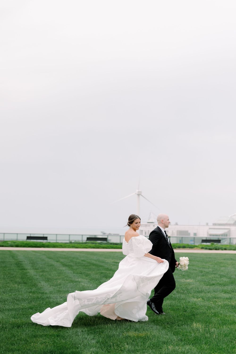 Wedding couple playfully running across a green lawn in formal attire.