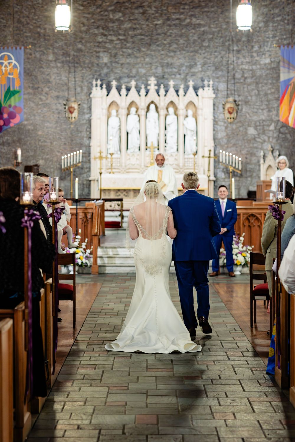 Bride in white gown walks down church aisle with escort toward altar during wedding ceremony.