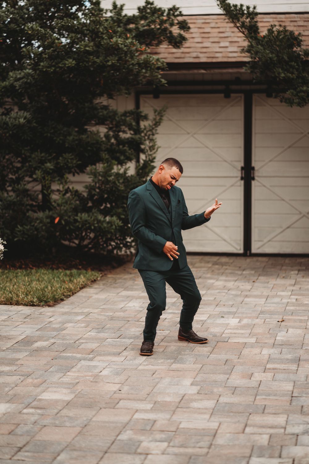 Man in emerald green suit dances joyfully on stone patio outside rustic venue.