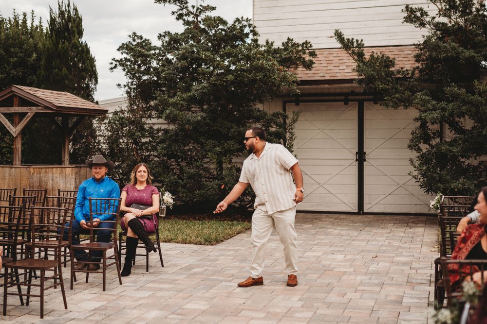 Wedding guest performs dance moves on stone patio while others watch from wooden chairs.