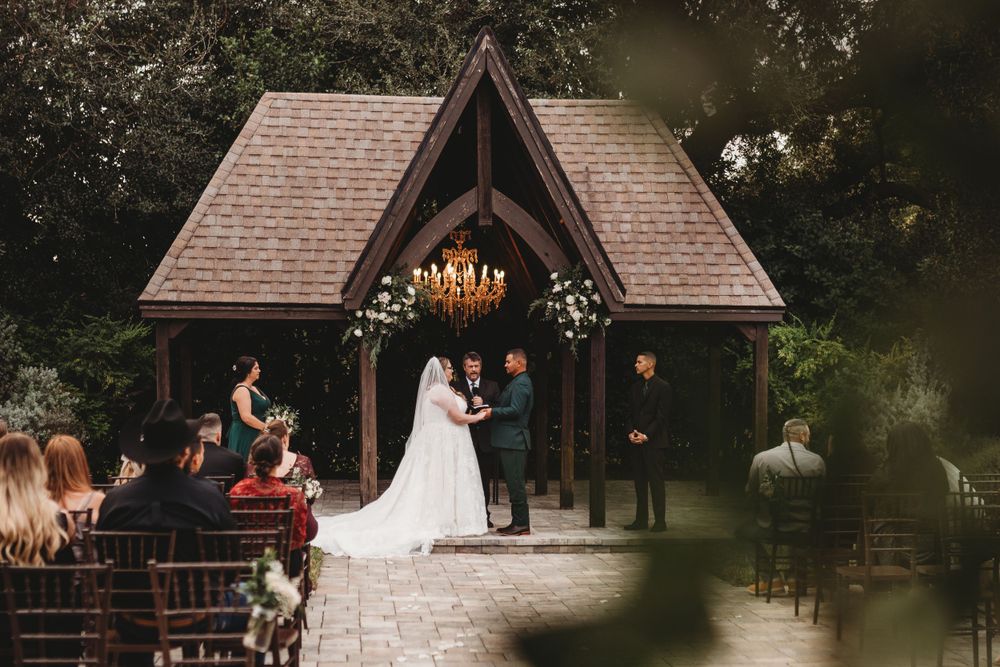 Wedding ceremony taking place in a rustic wooden chapel with chandelier and gathered guests on benches.