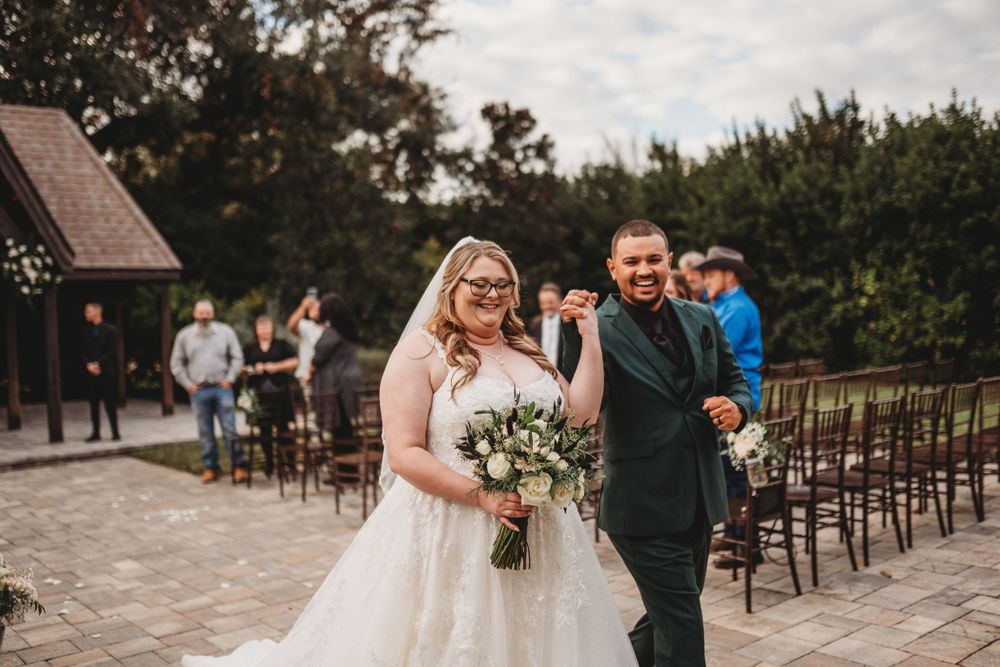 Newlyweds celebrating with bouquet while walking down stone path near outdoor chapel.