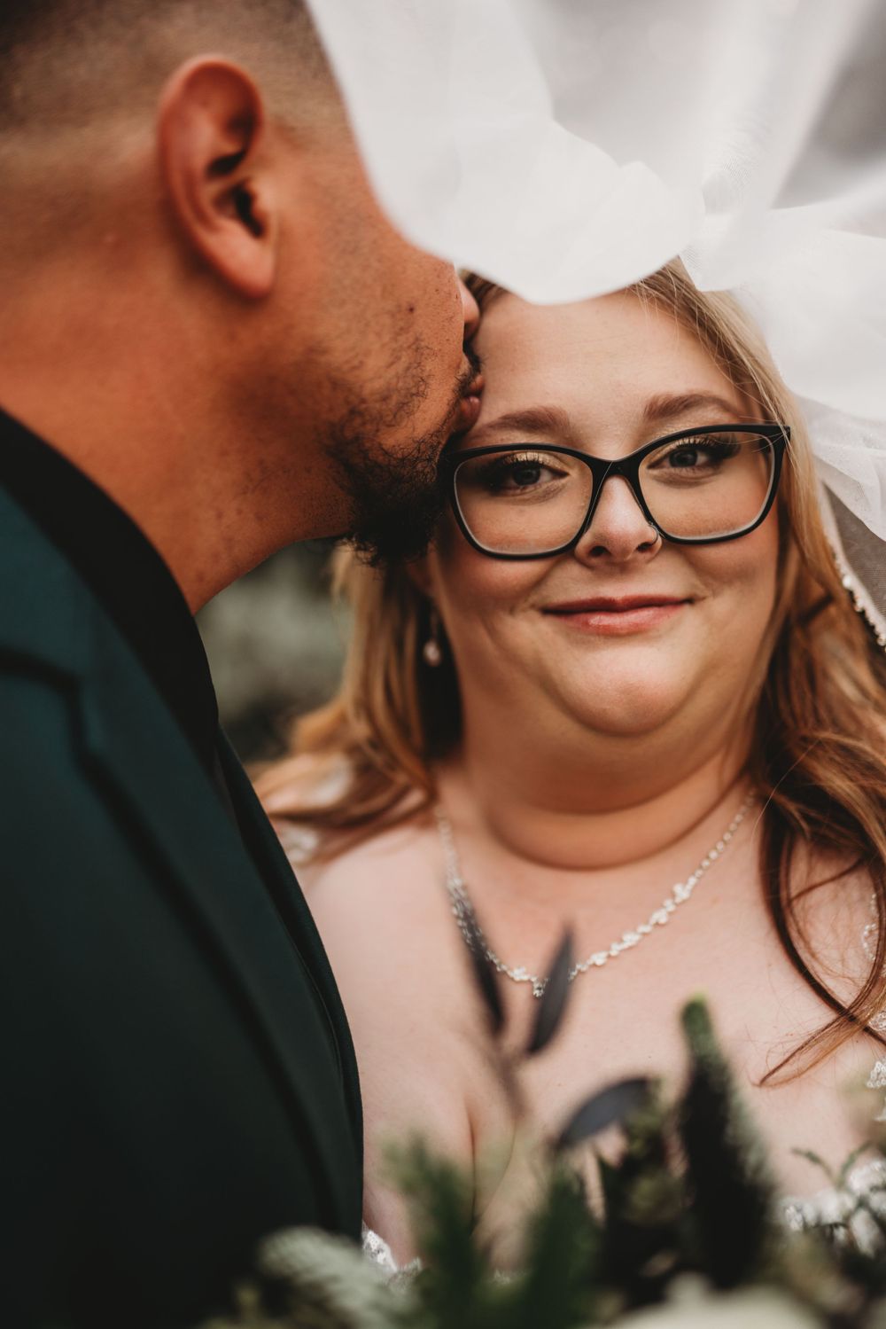 Intimate wedding portrait moment under crystal chandelier and wooden beams.