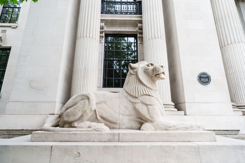 White stone lion statue guards the entrance of a grand building with classical columns.