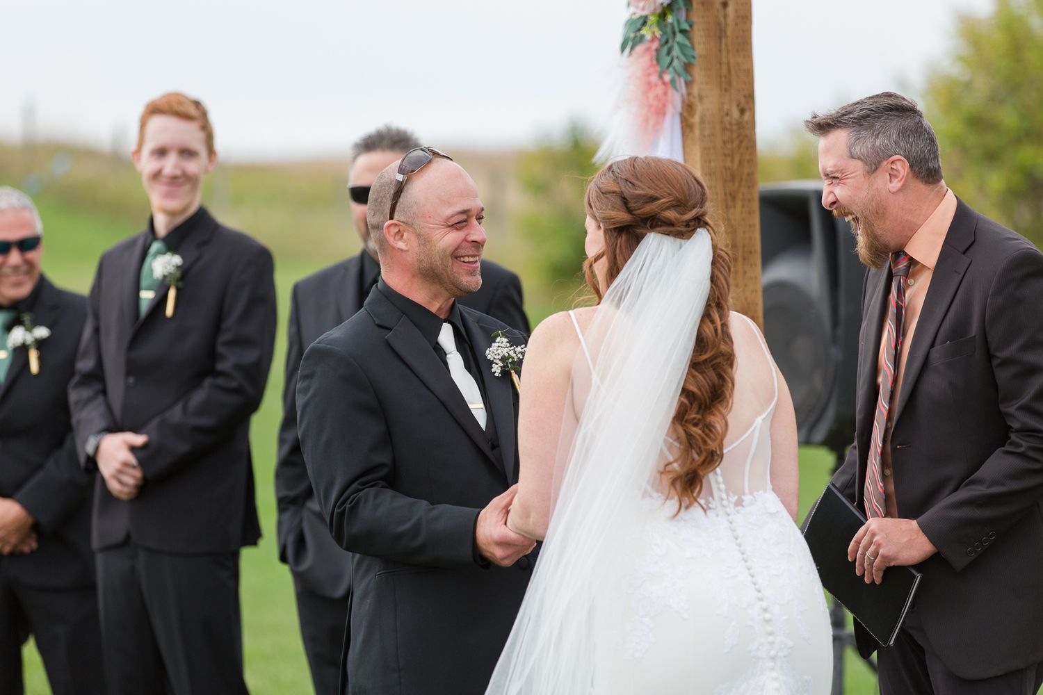 Outdoor wedding ceremony under autumn skies with wedding party in black suits.