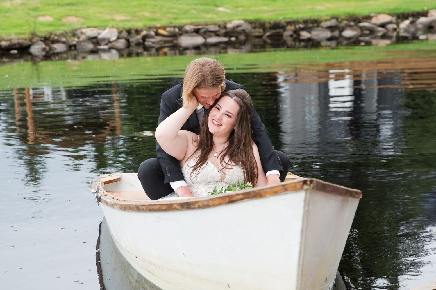 Romantic couple sitting in white rowboat on tranquil pond with natural reflection.