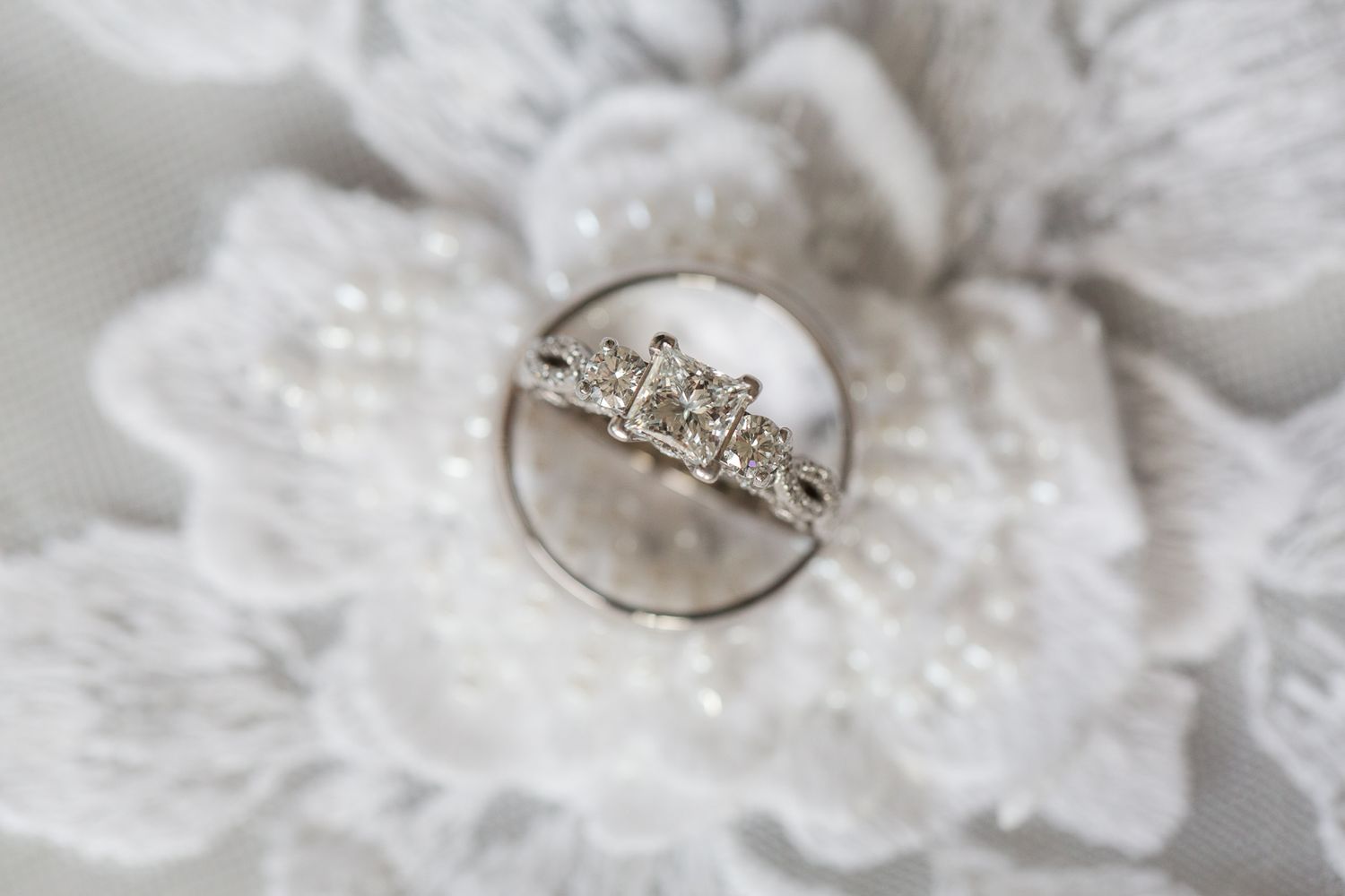 A sparkling engagement ring nestled on a white lace floral surface.