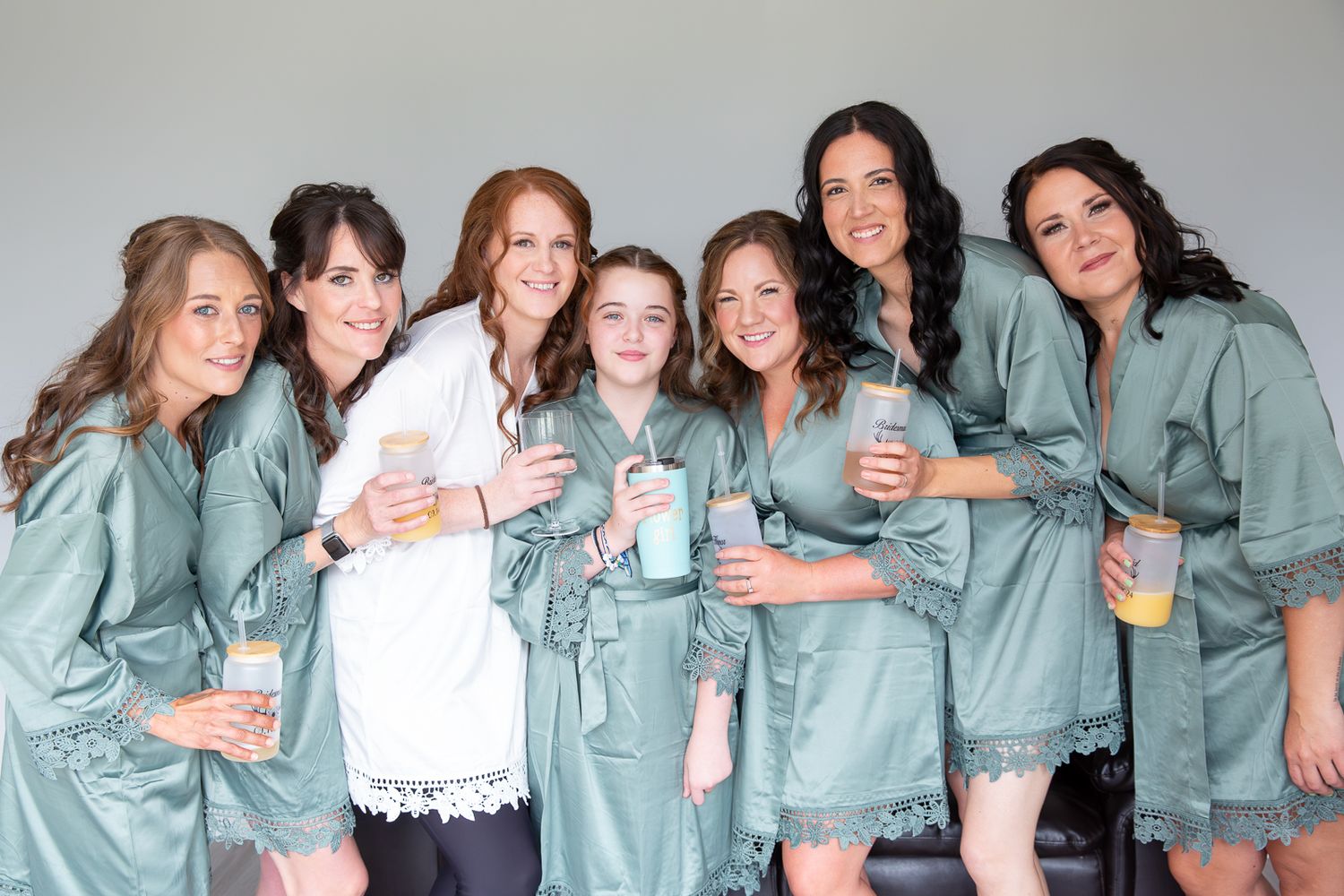 A group wearing matching sage green robes poses together for a pre-wedding photo.