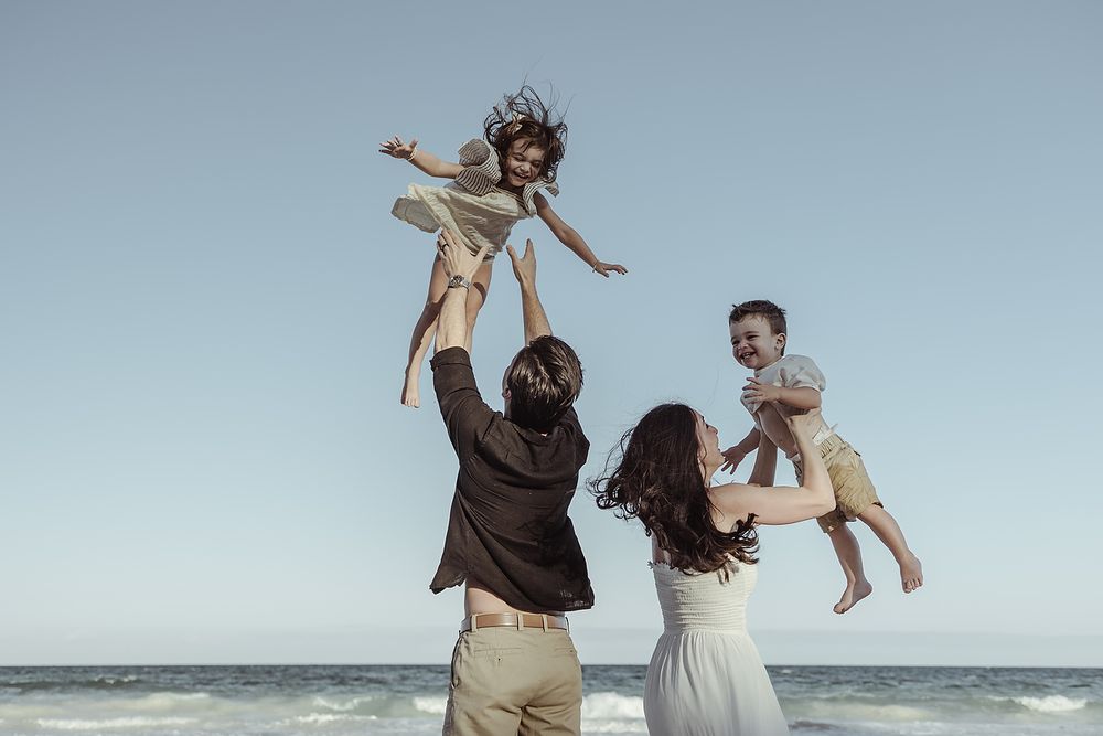 Parents lifting children in the air during joyful beach family photoshoot at La Zebra Hotel, Riviera Maya.