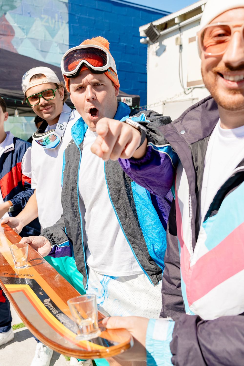 Group of men in retro ski gear and goggles at an outdoor après-ski party event.