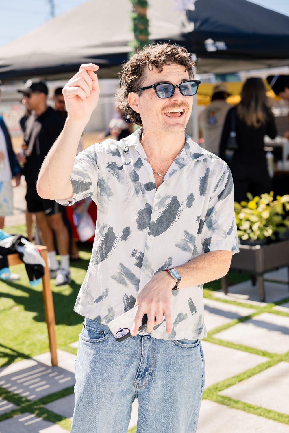 Smiling man in patterned shirt and sunglasses enjoying a sunny outdoor festival.