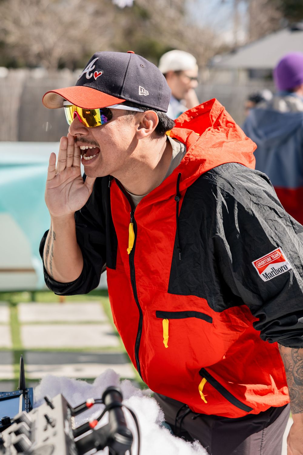 Man in red ski jacket shouting with hand cupped to mouth at outdoor event.
