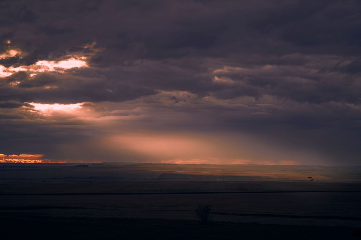 Dramatic sunset sky with dark clouds and golden sunbeams breaking through over a silhouetted horizon photographed by Evan Will in Alberta