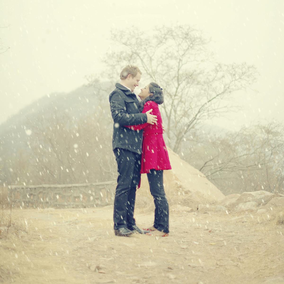 A romantic winter scene with a couple embracing as snow falls around them.
