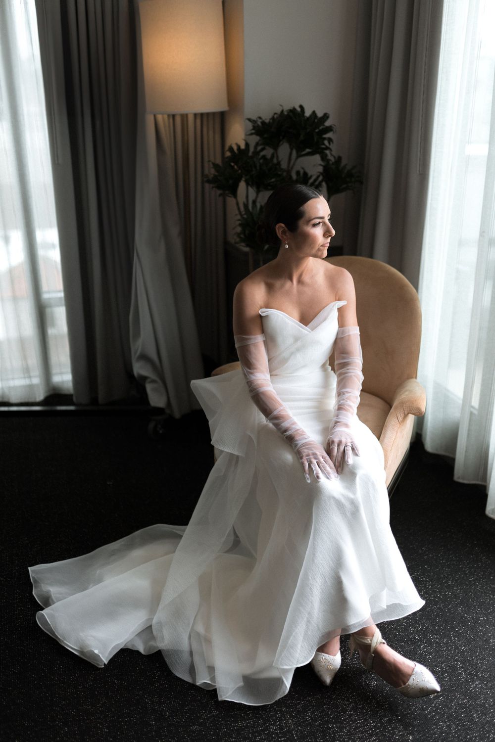 An elegant portrait of someone in a white wedding gown sitting by a window in soft natural light.