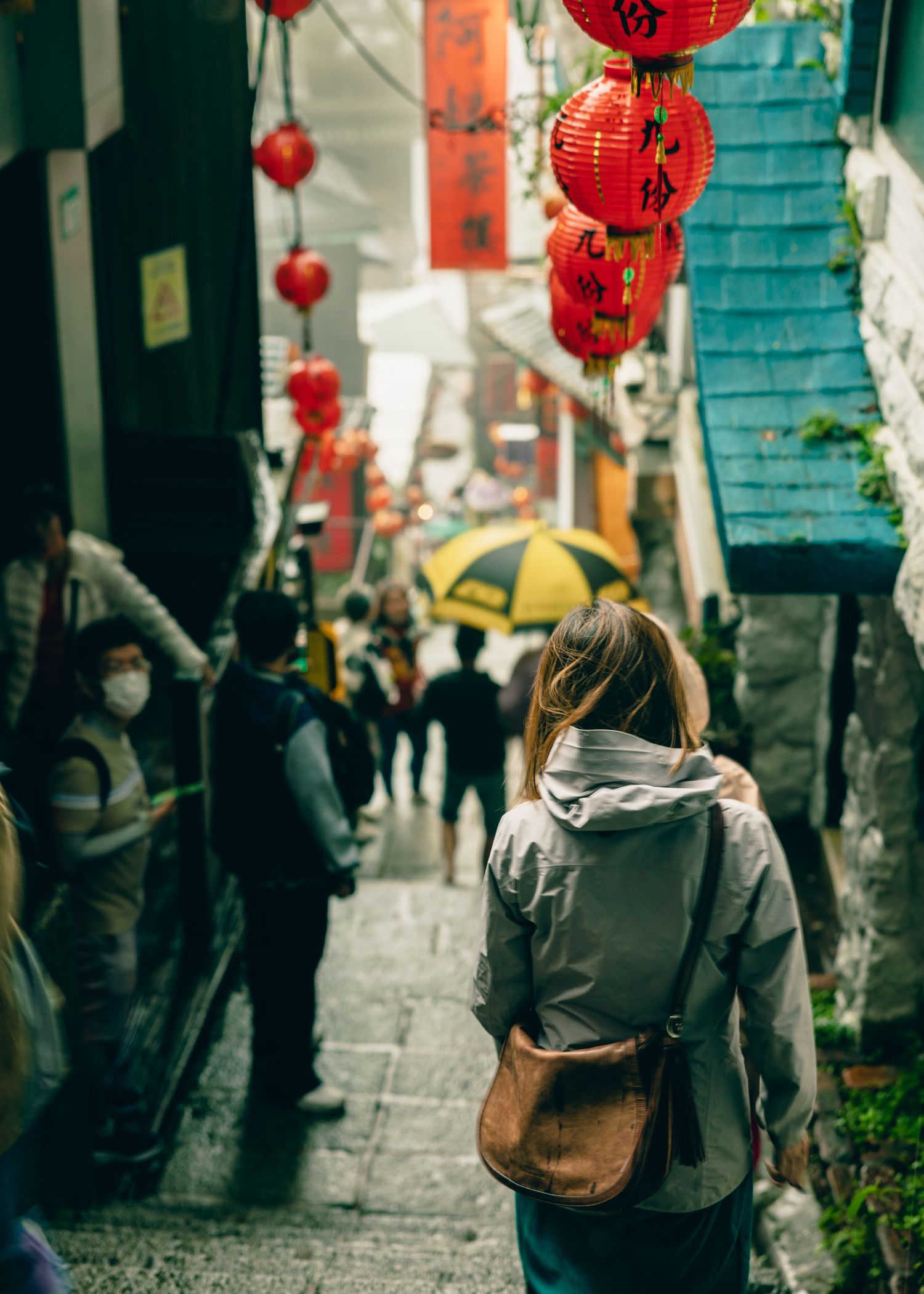 Traditional red paper lanterns hang above a narrow stone street in an Asian city district.