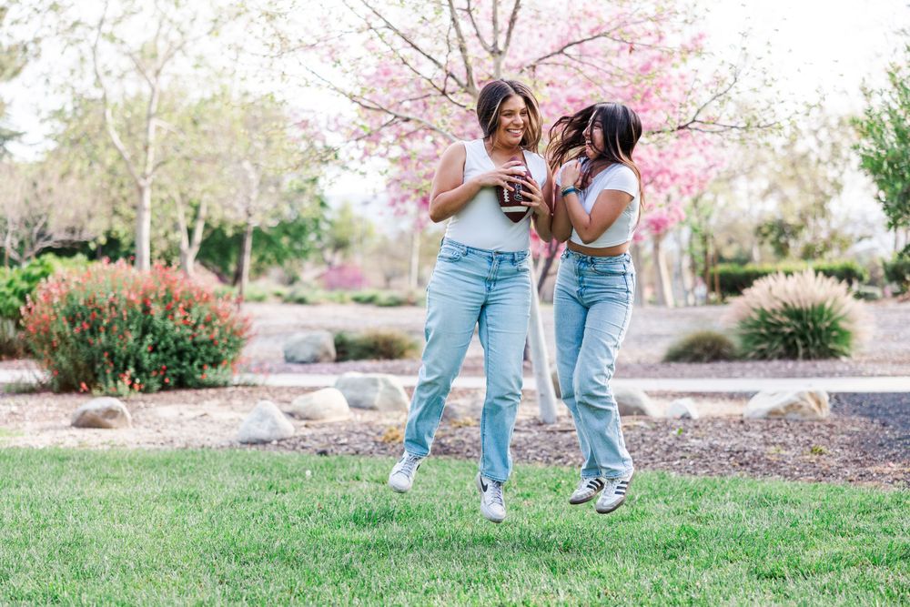 Two friends share a laugh while enjoying drinks in a spring garden with blooming cherry blossoms.