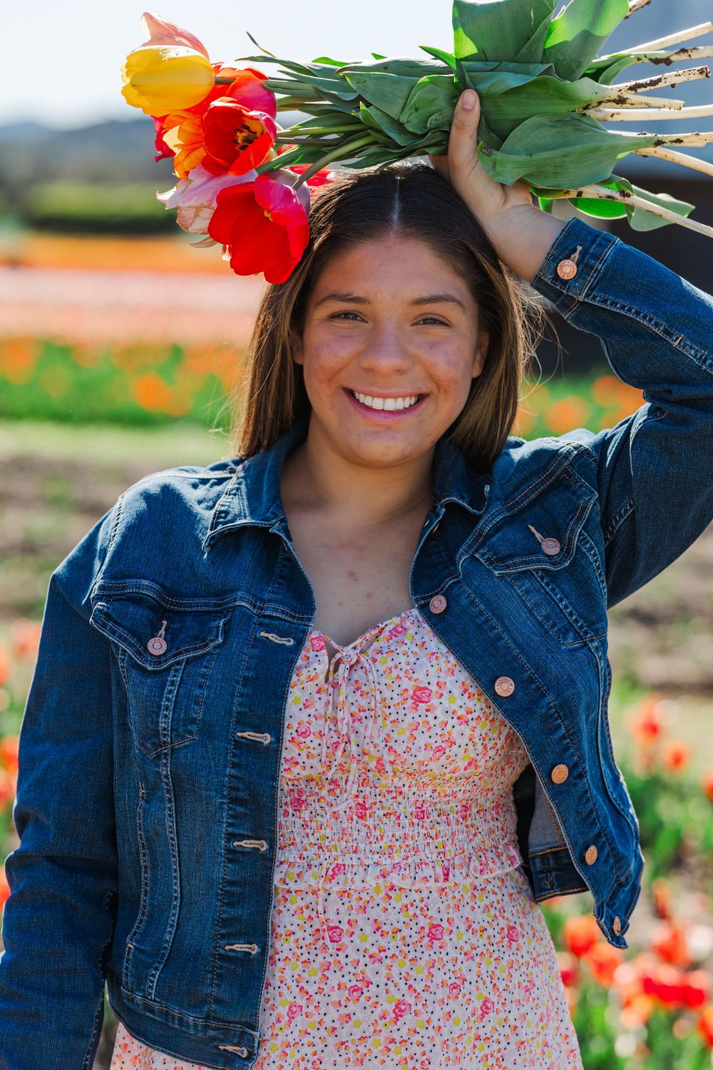 A denim jacket and floral dress create a spring look among colorful tulips and greenery.