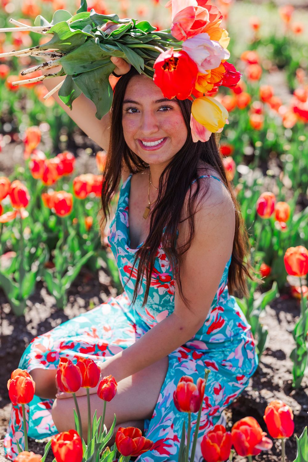 Person wearing floral crown and dress sitting among blooming red tulips.