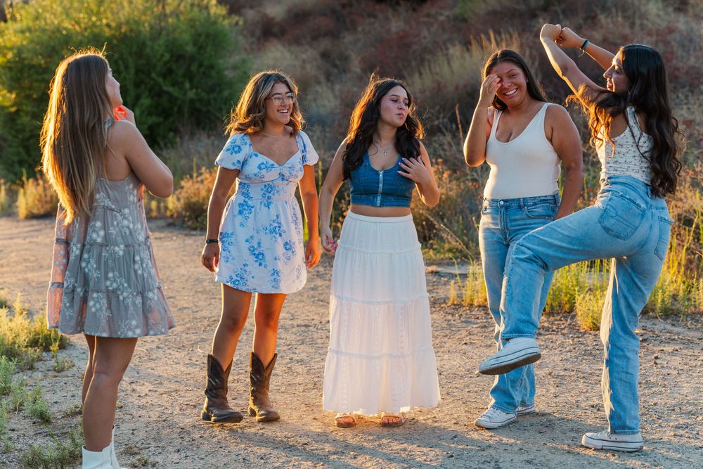 Friends dancing and having fun outdoors during golden hour in casual attire.