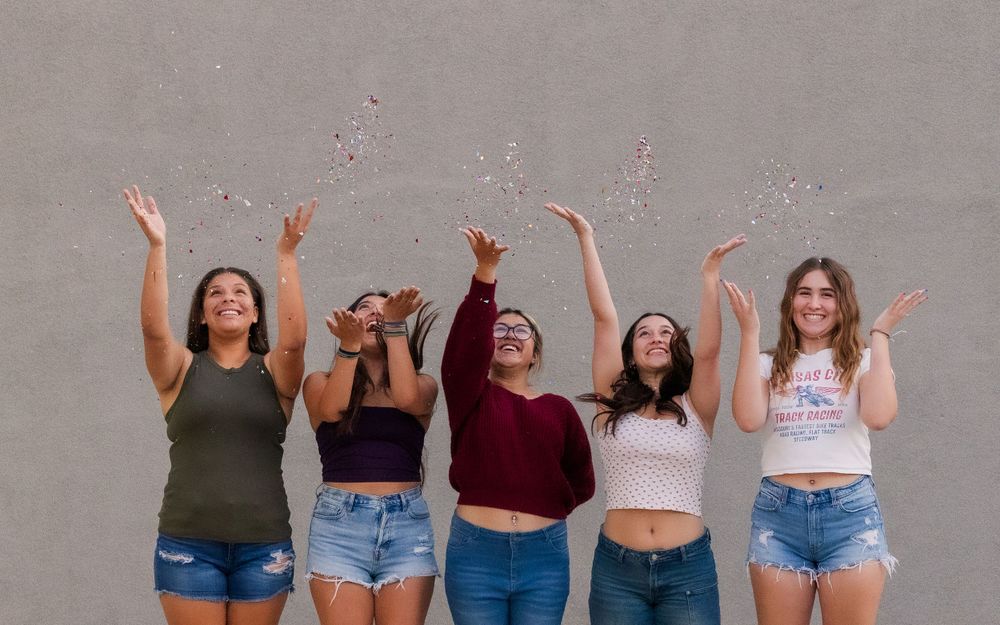 Friends throwing confetti in the air against grey wall background.