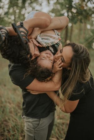 Mother playfully embracing and tickling child in outdoor forest setting during golden hour.