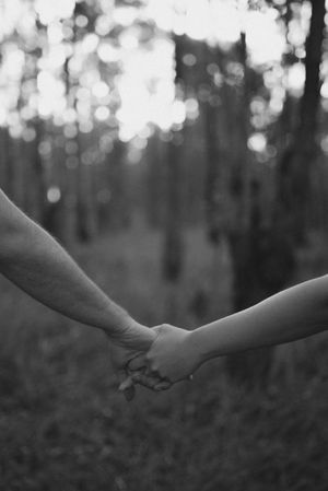 Two people holding hands in black and white photo with blurred forest background.