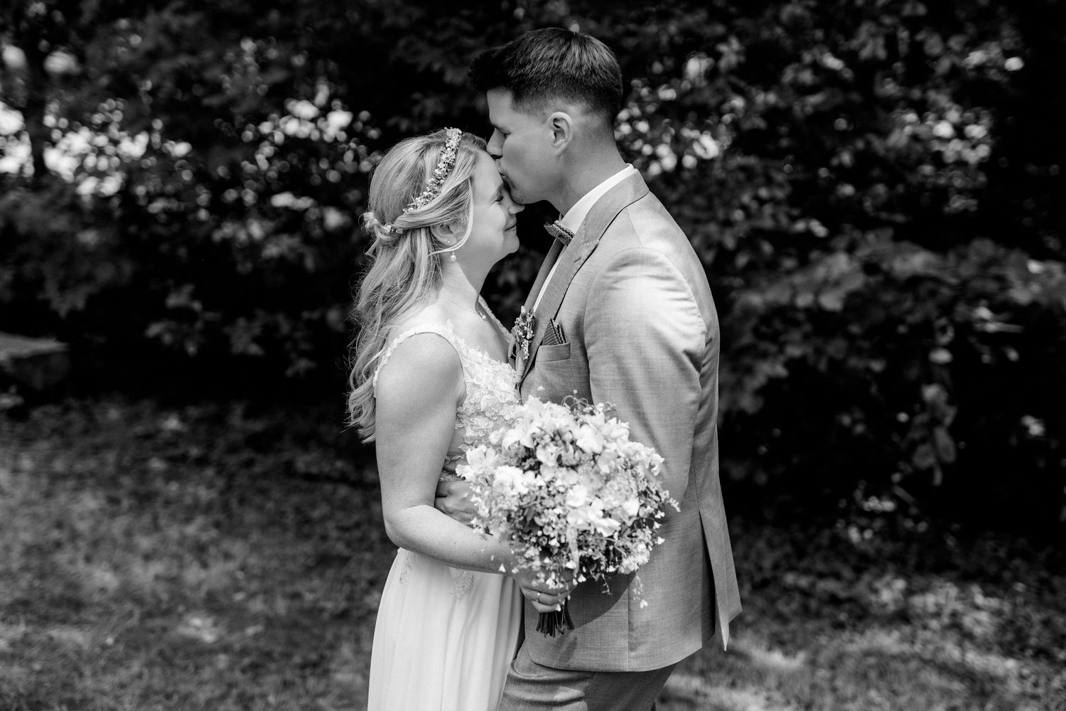A black and white wedding portrait of a couple sharing a tender moment outdoors.