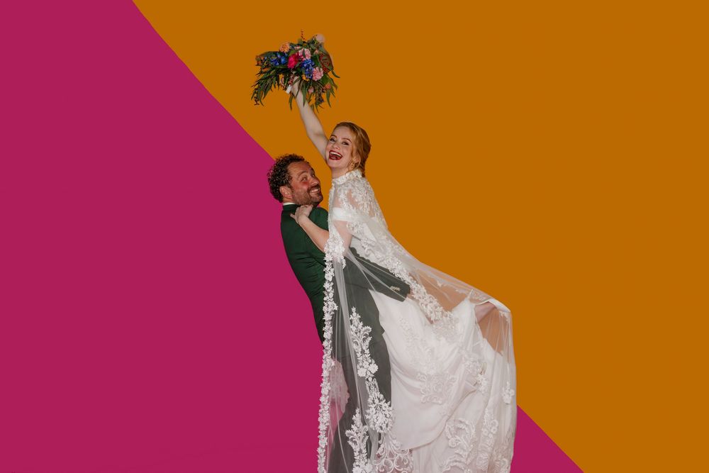 Originele on trend trouwfoto van een blij bruidspaar voor een graphische oranje-roze backdrop.
