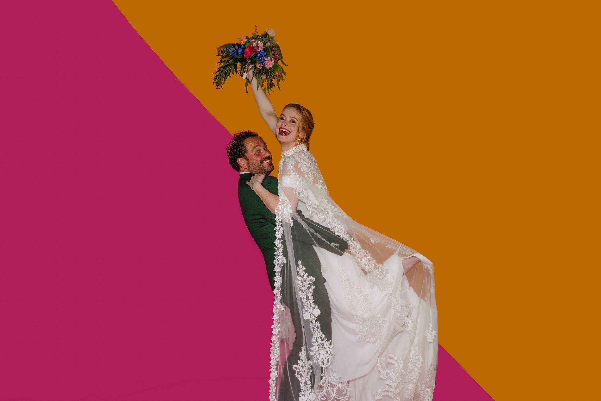 Originele on trend trouwfoto van een blij bruidspaar voor een graphische oranje-roze backdrop.