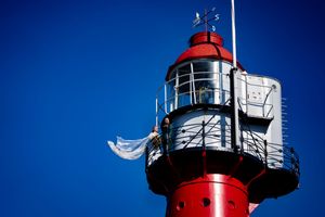Trouwfoto van een bruidspaar op een vuurtoren in Hoek van Holland. De bruid draagt een witte trouwjurk met prachtige kanten cape.