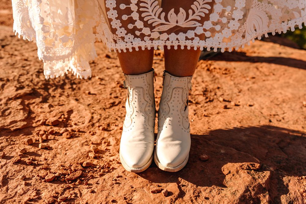 Vintage-inspired wedding boots and lace dress hem detail on Sedona red desert soil.