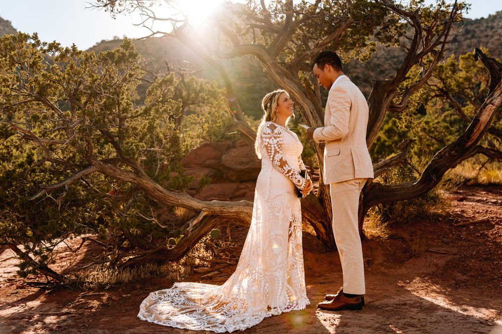 Wedding couple poses in beautiful Sedona desert setting with sunburst behind them.