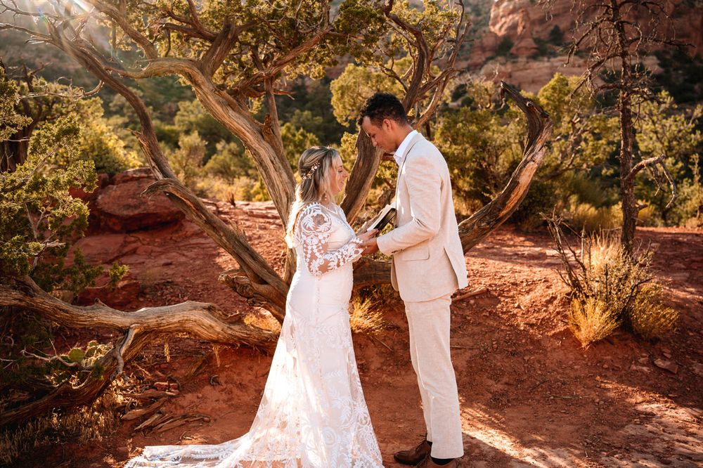 A celebratory moment between newlyweds on Sedona red desert soil with twisted trees in background.