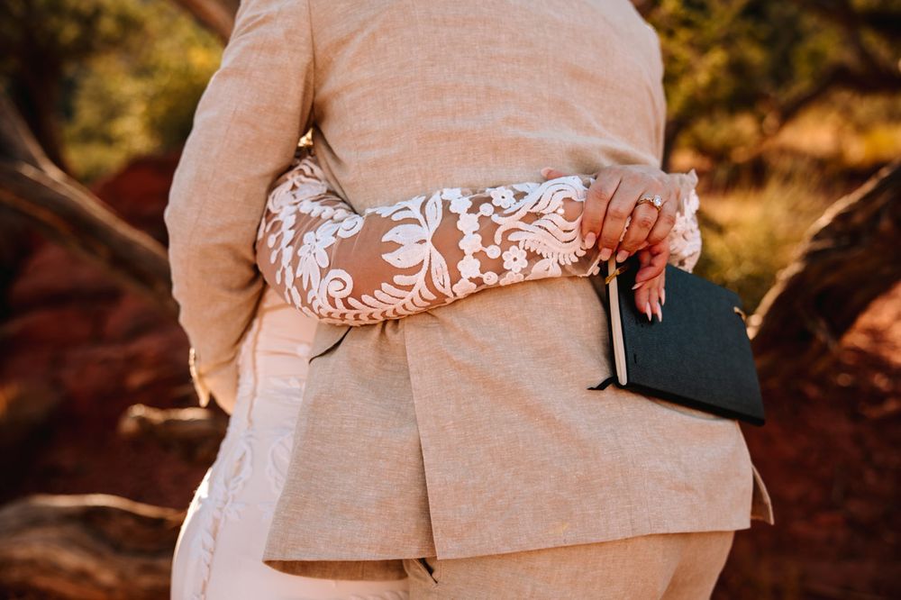 Close-up detail of a lace wedding dress and beige suit in golden Sedona desert light.