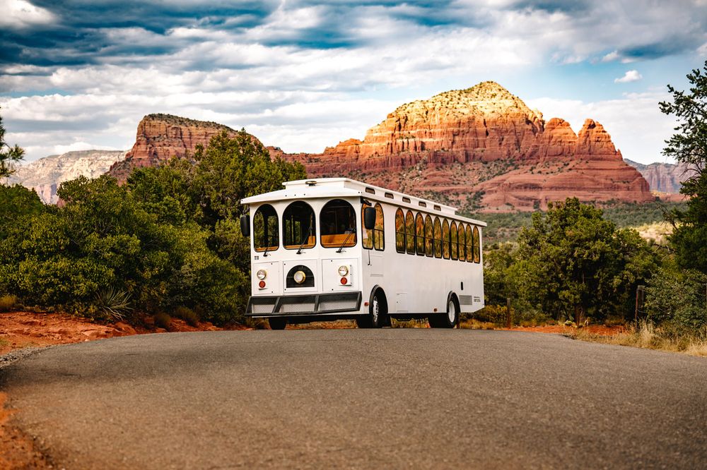A white wedding trolley bus parks on a scenic road with majestic Sedona red rock formations in the background.