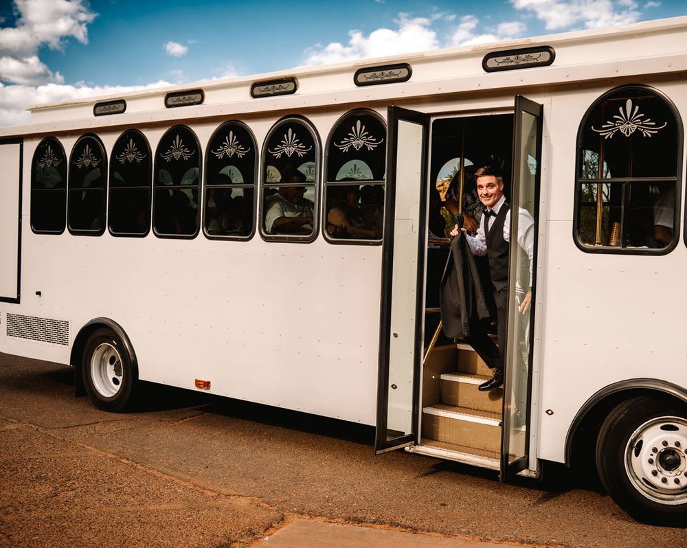 A white wedding trolley bus with decorative windows stands parked in the Sedona desert landscape.